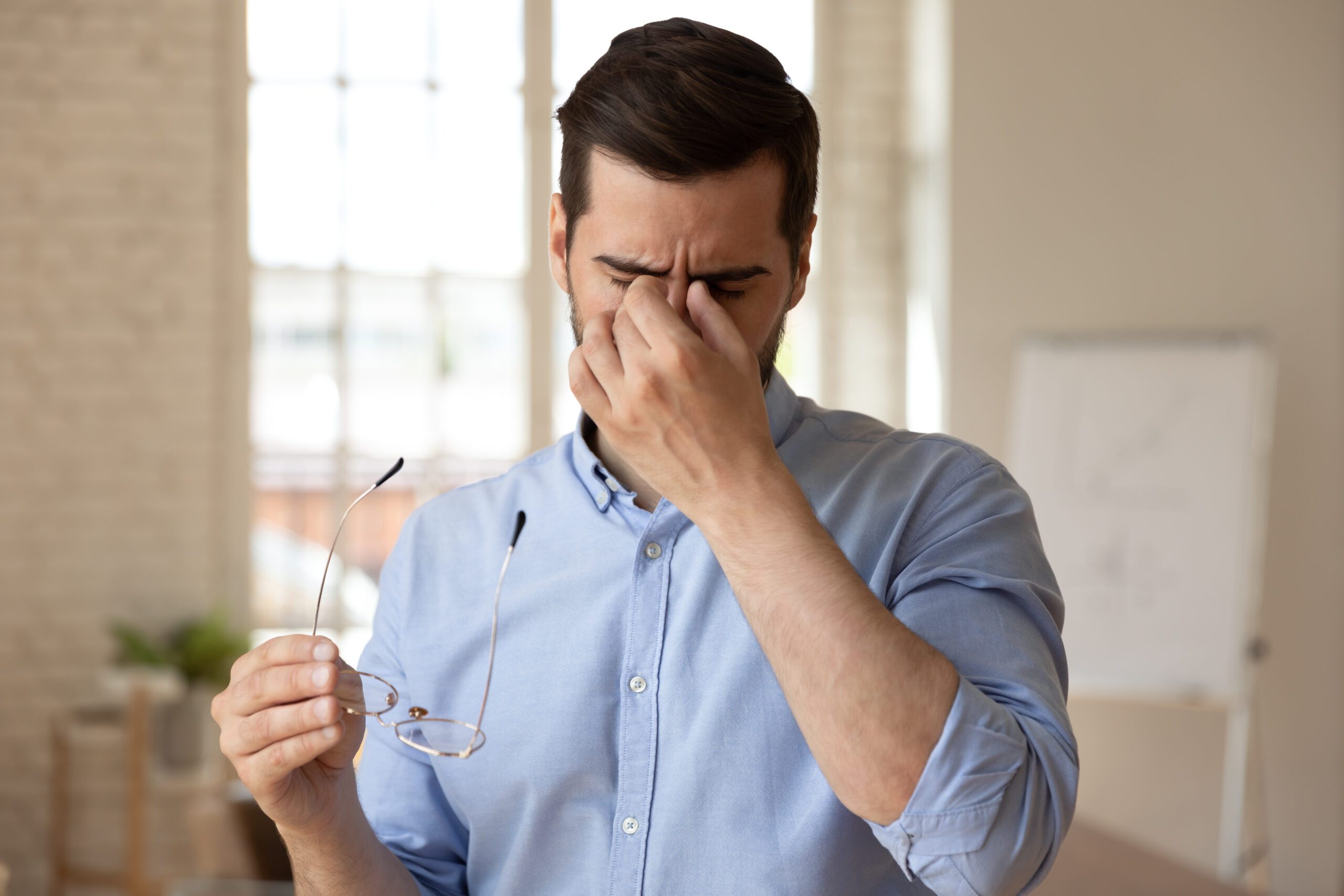 A tired man rubs his eyes while holding glasses, reflecting fatigue and the need for energy without relying on coffee.