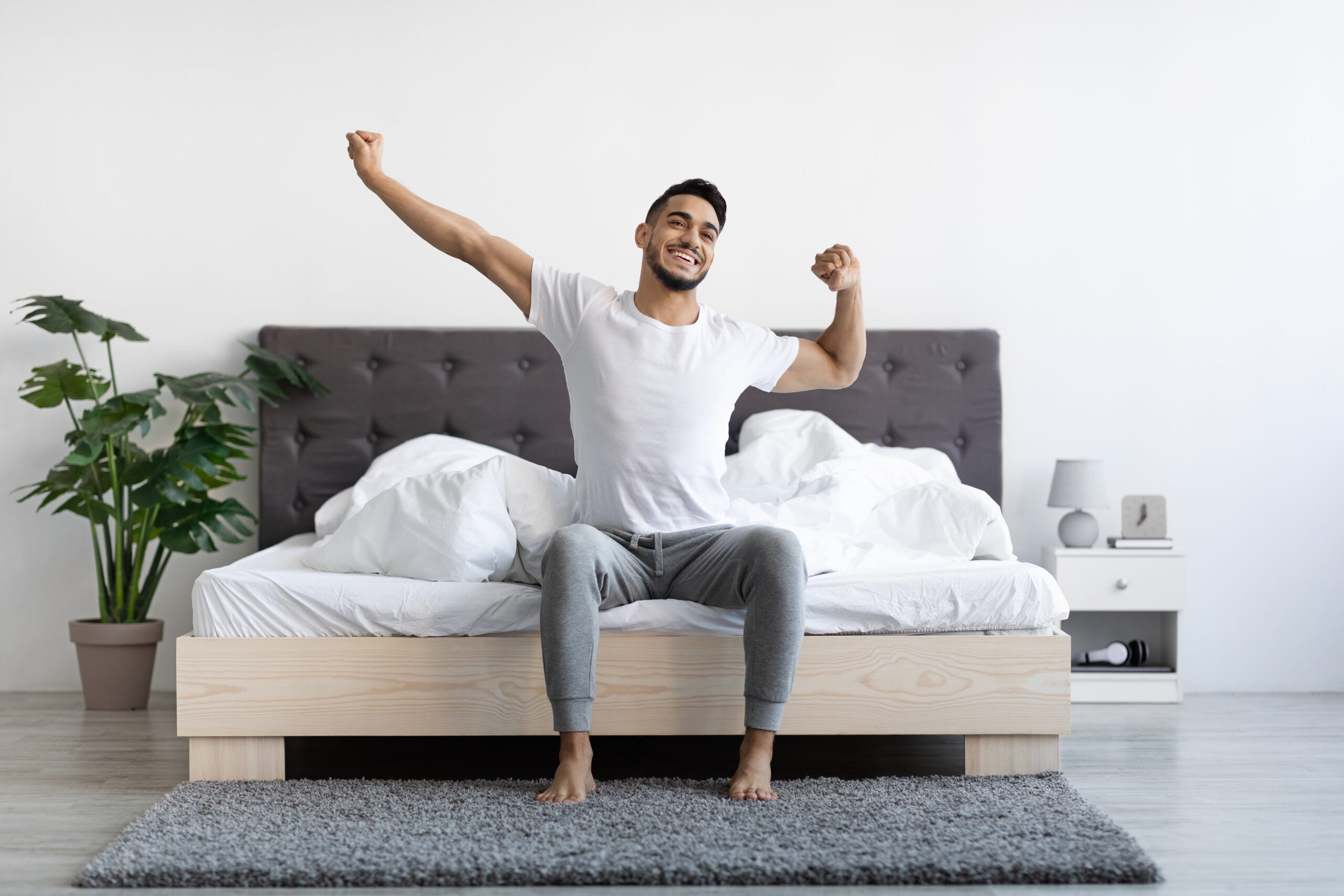 A man stretches happily on his bed in the morning, illustrating a simple routine for better energy.