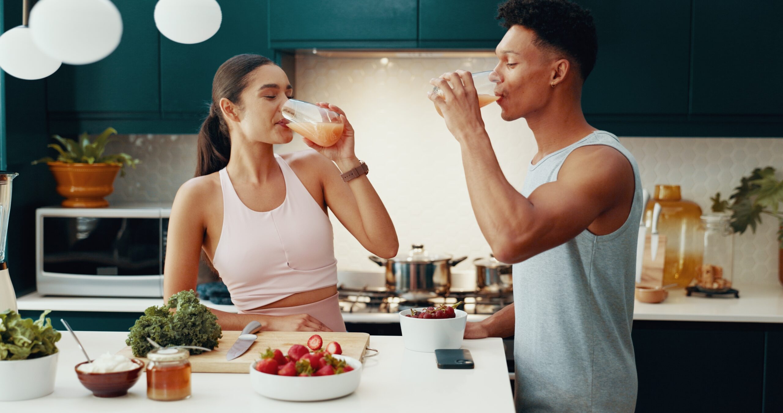 A sporty couple drinks healthy smoothies in the kitchen, surrounded by fresh ingredients, highlighting the connection between gut health and mood.