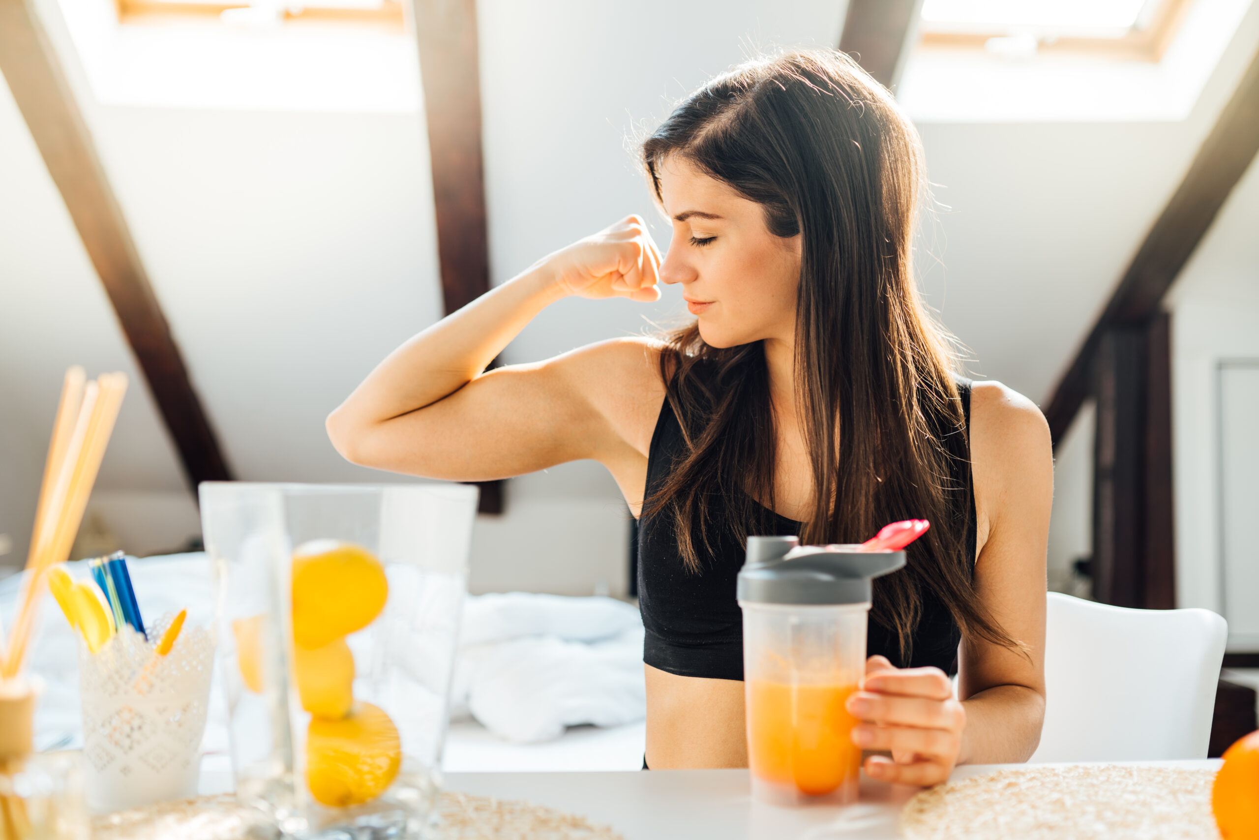 A woman confidently flexes her bicep while holding a smoothie, symbolizing natural ways to boost immunity beyond supplements.