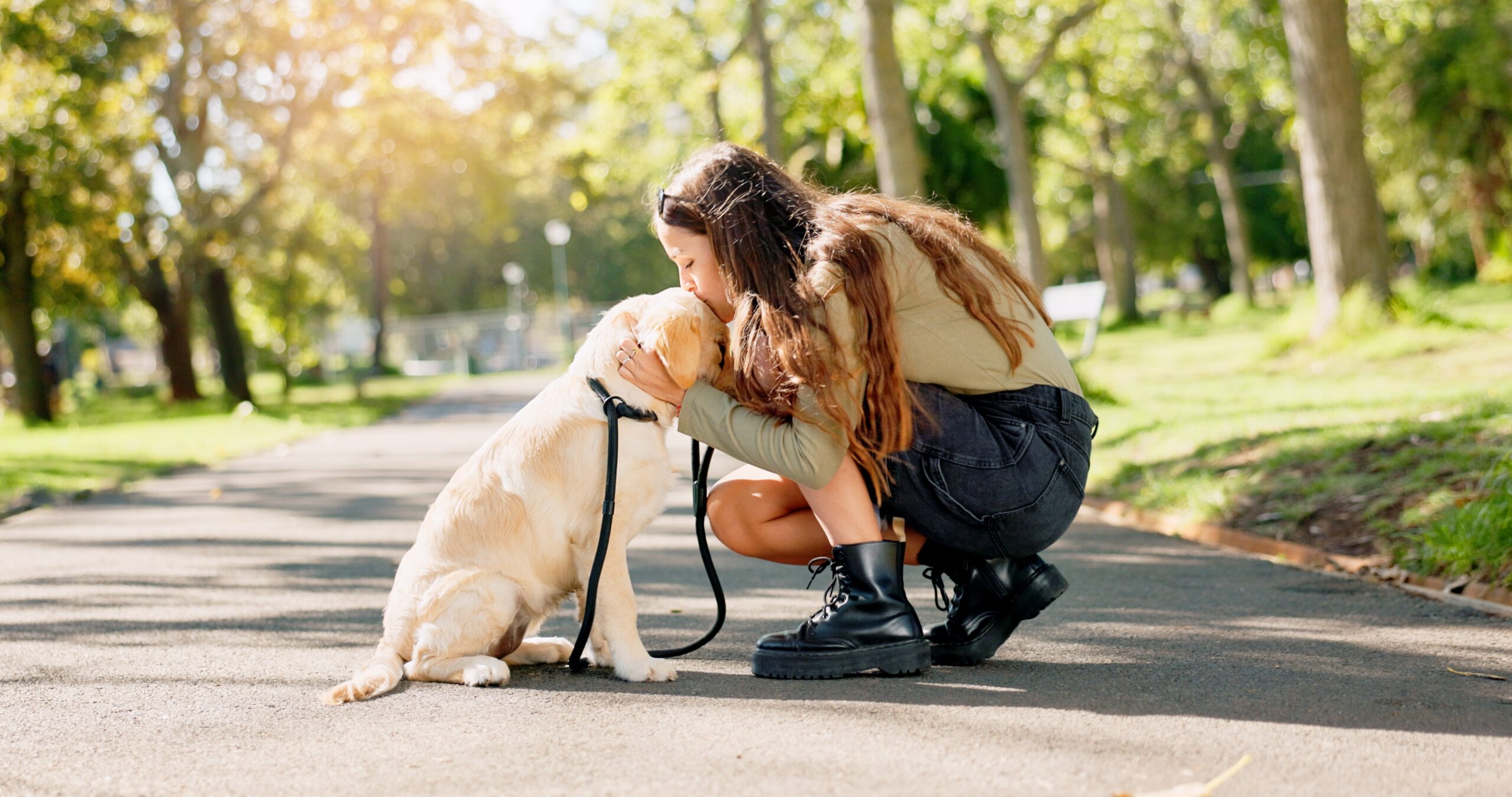 A woman kneels to hug her dog during a walk in the park, highlighting the benefits of daily walking.